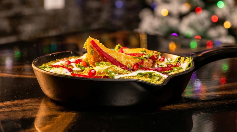 Crispy golden tacos in a hot skillet with creamy sauce, herbs, and pomegranate seeds.