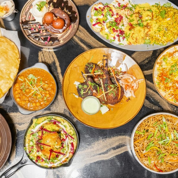 A vibrant spread of Indian food, including curries, bread, biryani, noodles, and dessert, on a dark table.