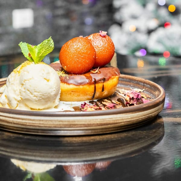 Dessert plate with chocolate-glazed donut, gulab jamuns, vanilla ice cream, mint, and rose petals.