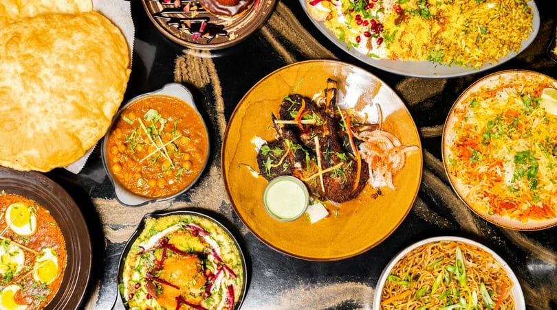 Overhead view of a vibrant spread of Indian dishes including curries, flatbread, lamb chops, and rice.