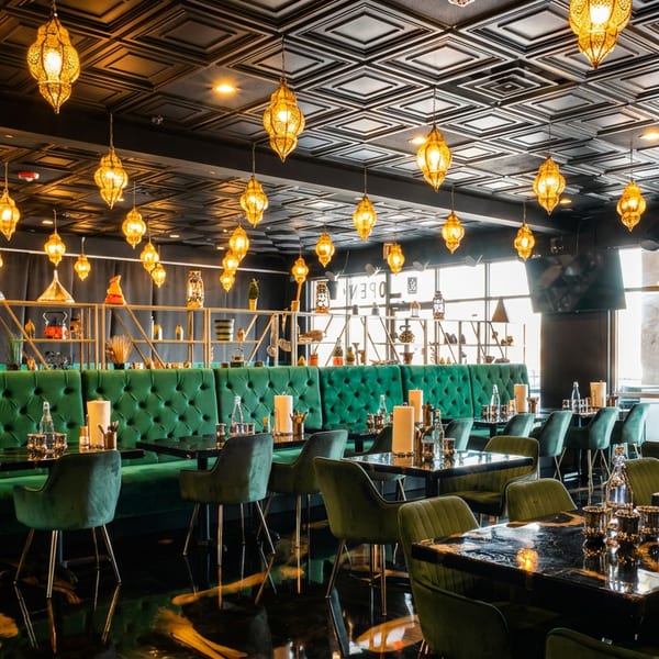 Elegant restaurant interior with green velvet booths, black tables, and many golden lanterns.