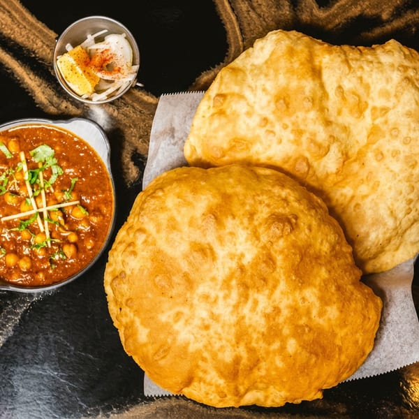 Chana masala with two fried flatbreads, garnished with cilantro, onions, and lemon on a dark table.