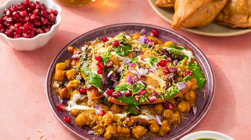 Indian chaat with chickpeas, crispy flatbread, green and white sauces, pomegranate, and red onions.