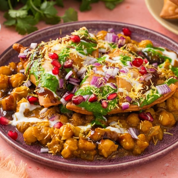 A vibrant plate of samosa chaat with chickpeas, chutneys, pomegranate, and red onions.