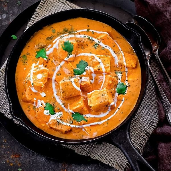 Delicious paneer butter masala in a cast iron skillet, garnished with cream and fresh cilantro.
