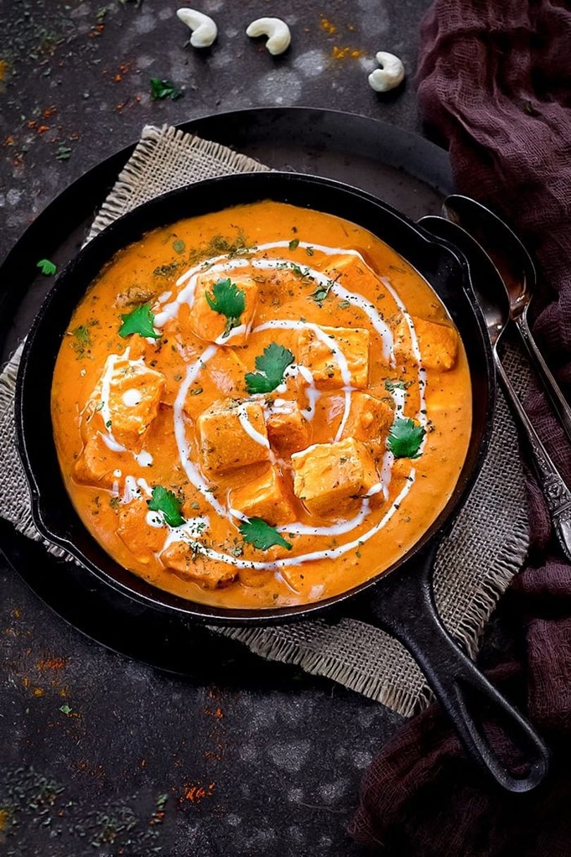 Delicious paneer butter masala in a cast iron skillet, garnished with cream and fresh cilantro.