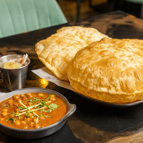 A bowl of chana masala with cilantro, two large bhature, and a side of lemon.