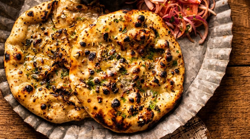 Two pieces of garlic naan bread with herbs and red onion salad on a metal plate.