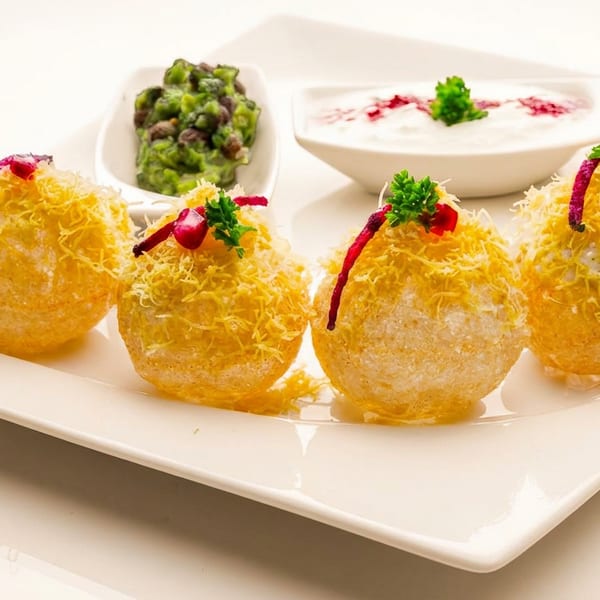 Golden pani puri topped with sev, herbs, and red garnish, served with green and white dips.