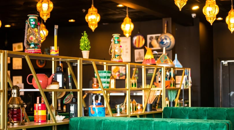 Vibrant restaurant interior with golden shelves displaying diverse decorative items and green velvet booth seating.