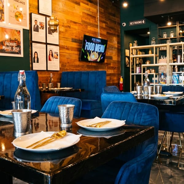 Stylish restaurant interior with blue velvet chairs, dark tables, and a digital menu on a wooden wall.