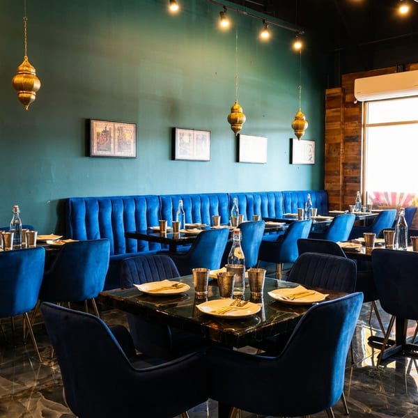 Restaurant dining room with blue velvet chairs, dark tables, teal walls, and golden hanging lamps.