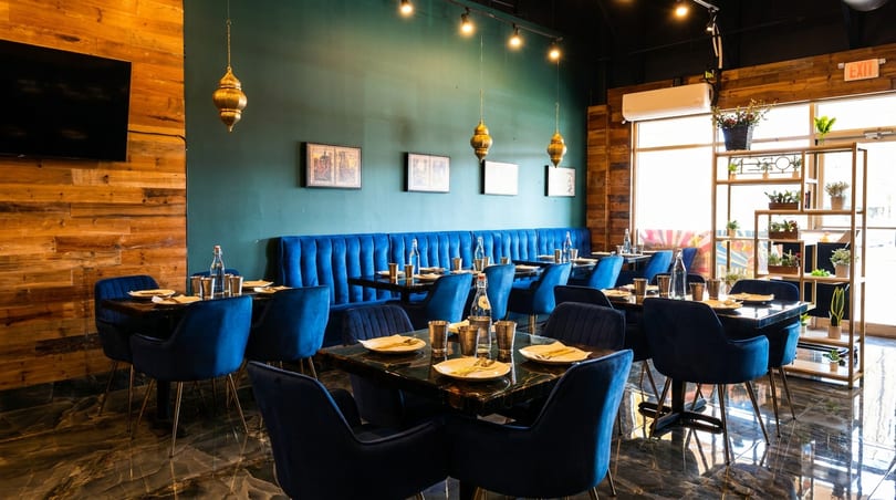 Elegant restaurant interior with blue velvet chairs, dark green walls, wooden accents, and set tables.