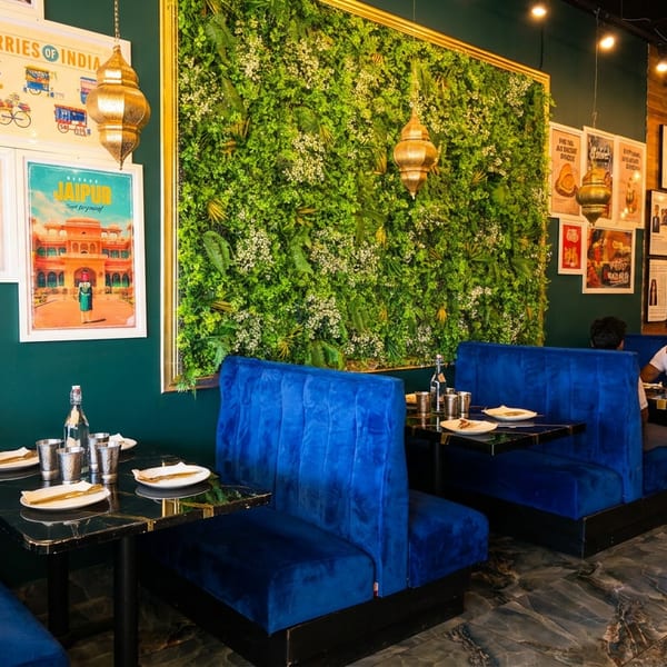 Vibrant restaurant interior with blue velvet booths, a large green wall, and Indian-themed artwork.