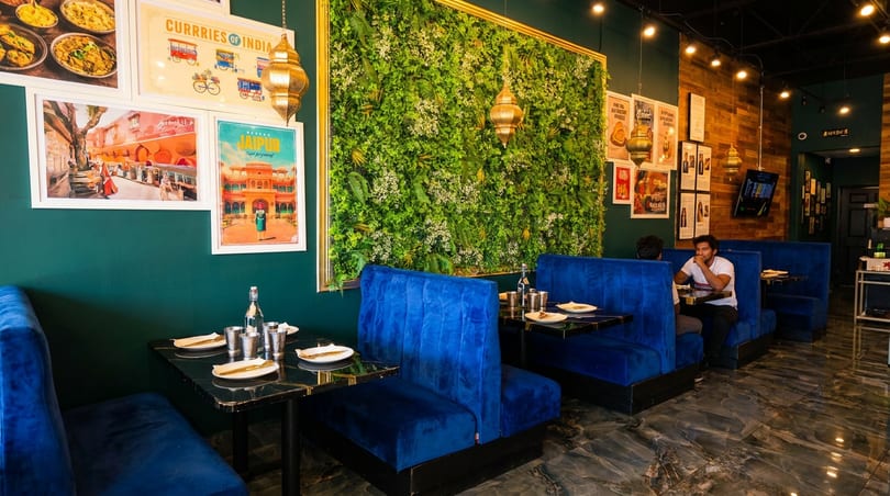 Modern Indian restaurant interior featuring blue booths, a lush green wall, and cultural artwork.
