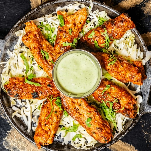 Grilled chicken kebabs on shredded cabbage with a green dipping sauce in a rustic pan.