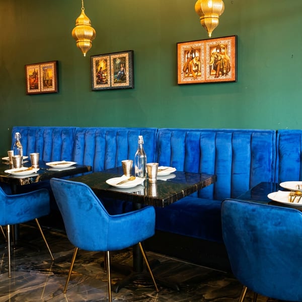 Vibrant restaurant interior with blue velvet seating, dark green walls, and traditional golden lamps.