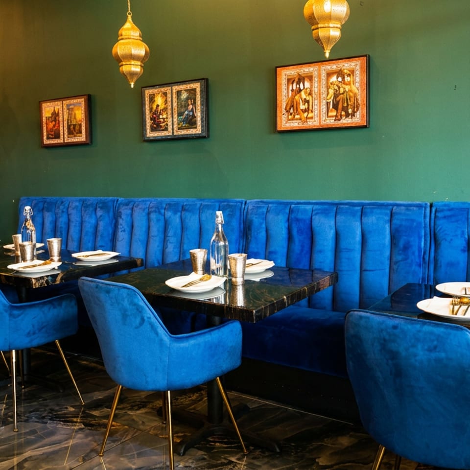 Vibrant restaurant interior with blue velvet seating, dark green walls, and traditional golden lamps.