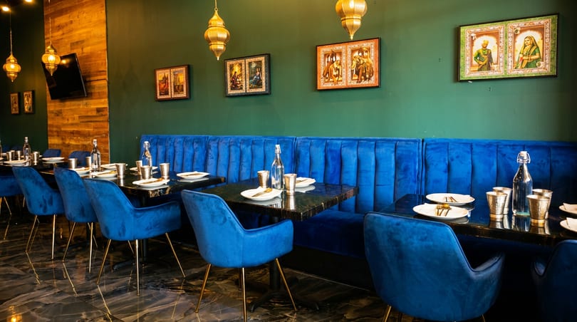 Vibrant restaurant interior with blue velvet seating, dark green walls, golden lanterns, and framed artwork.