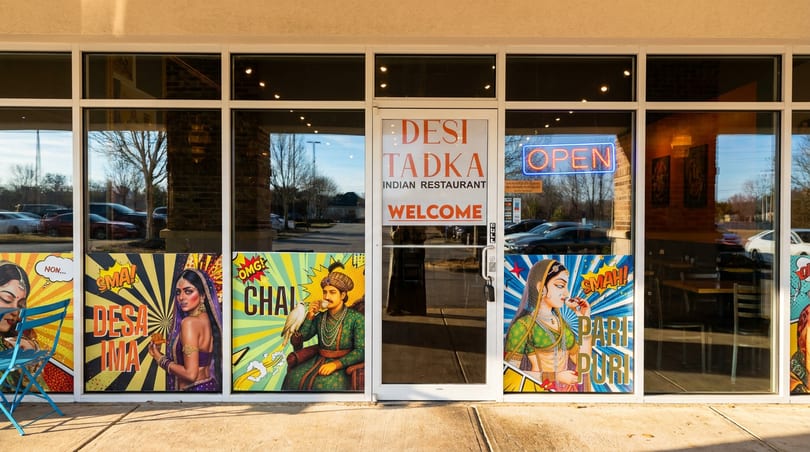 Desi Tadka Indian Restaurant storefront featuring vibrant pop-art window decals and an illuminated 'OPEN' sign.